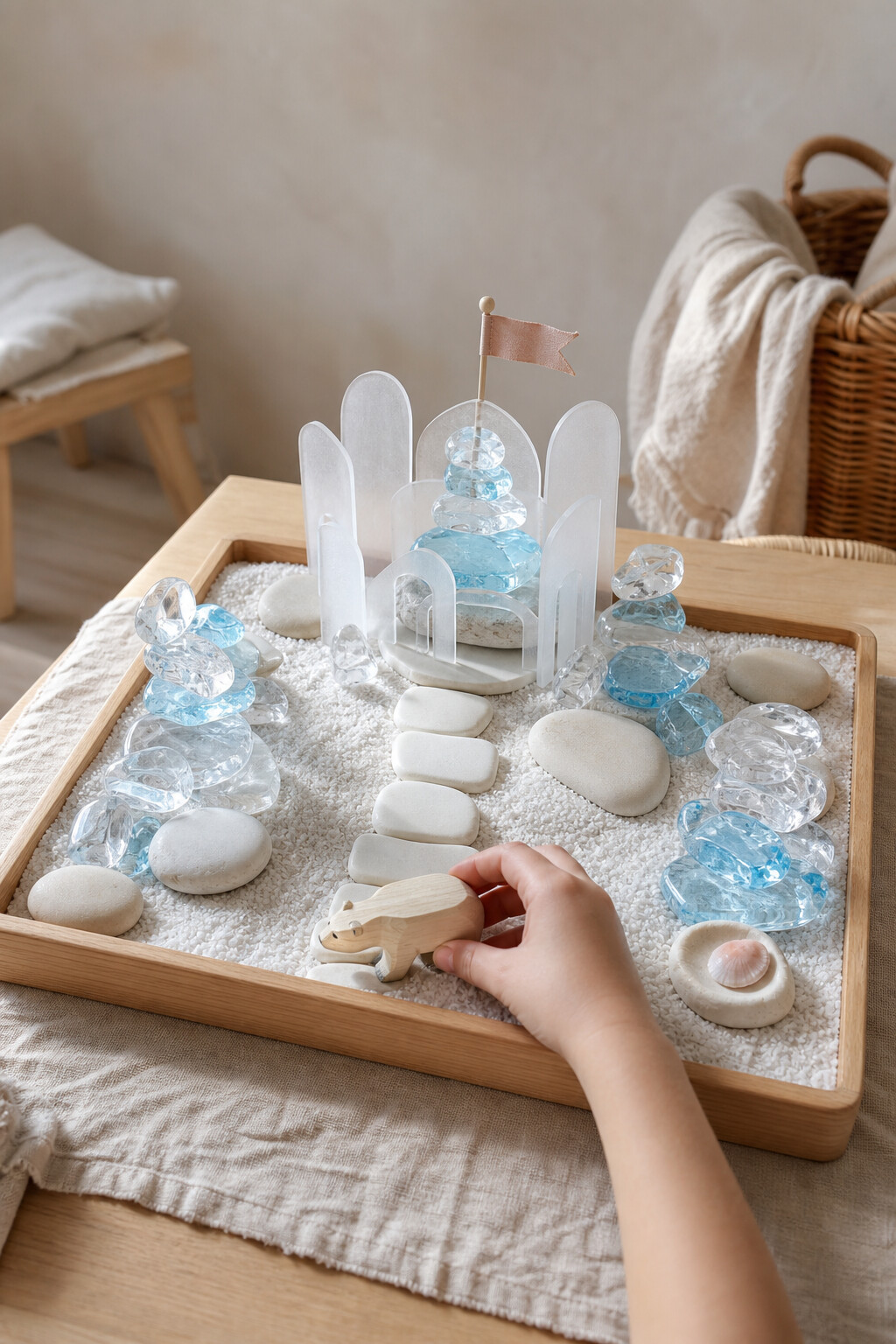 A white winter tray with clear and pale-blue crystals, stable arches, white stones and a wooden polar bear.